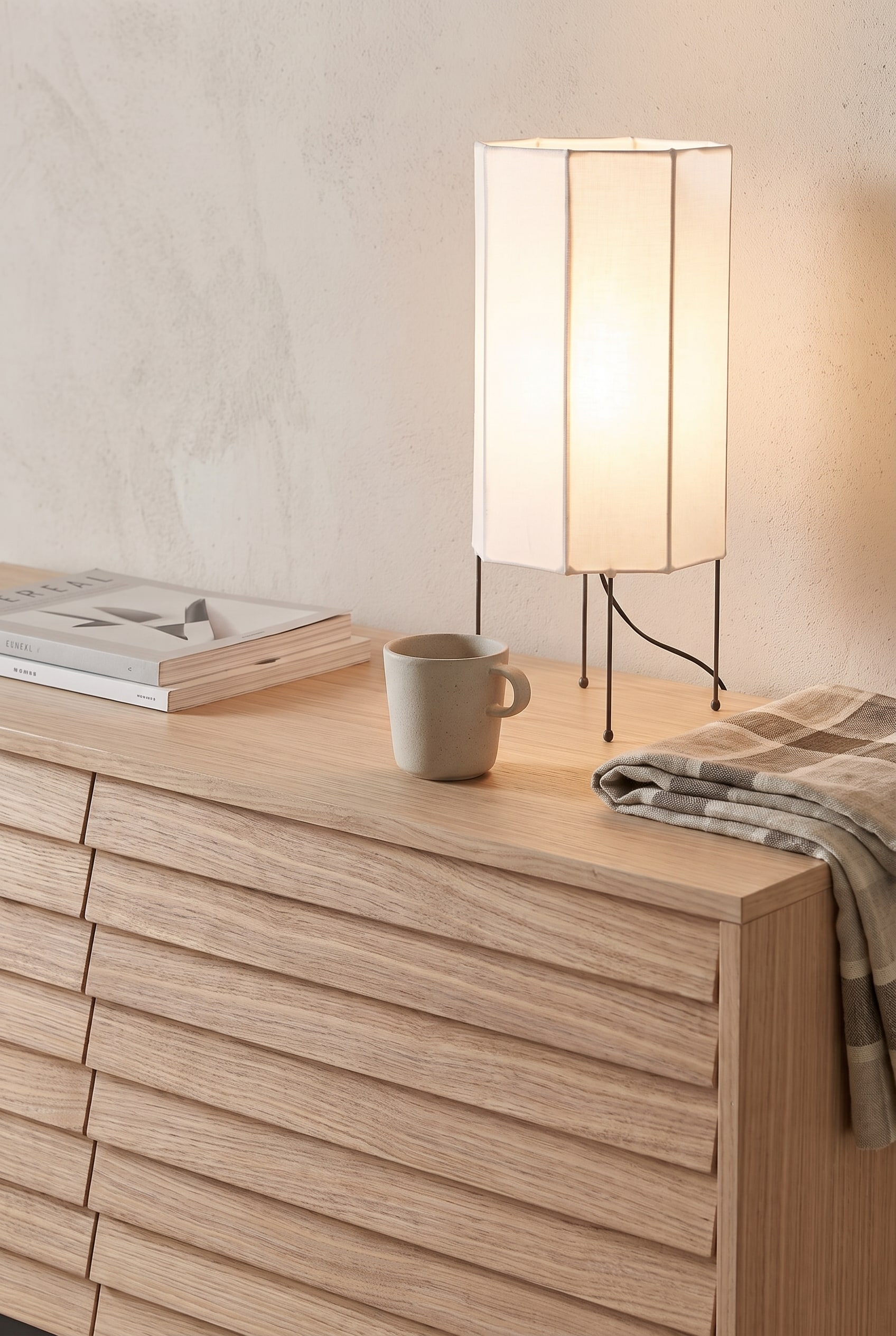 Dettaglio di un sideboard chiaro in legno di frassino con struttura a lamelle verticali, decorato con una delicata lampada di carta e un vaso di vetro.