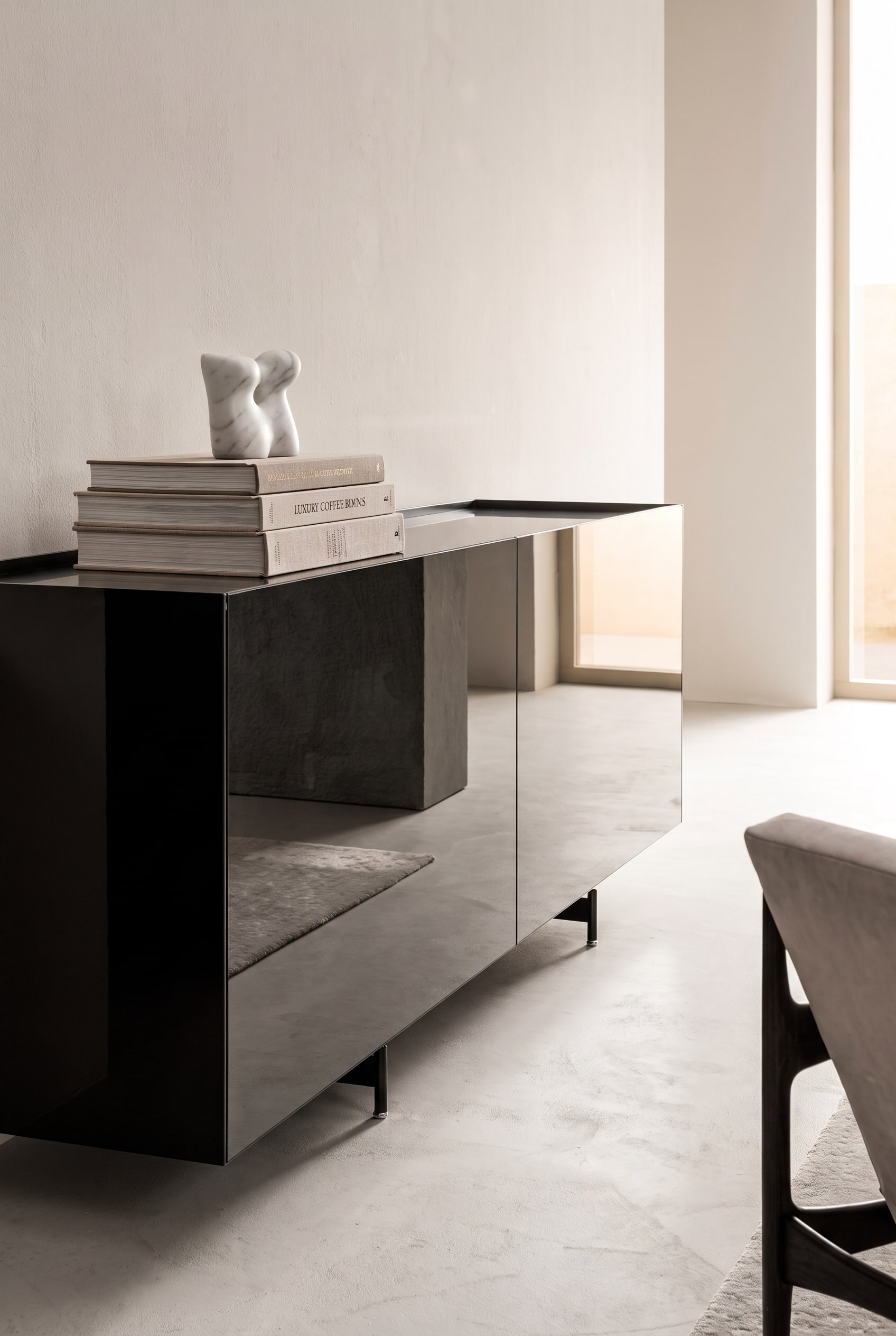 Sideboard mit verspiegelten Fronten, darauf ein ordentlicher Stapel aus drei gro&szlig;en Bildb&auml;nden, gekr&ouml;nt von einer kleinen wei&szlig;en Marmorskulptur