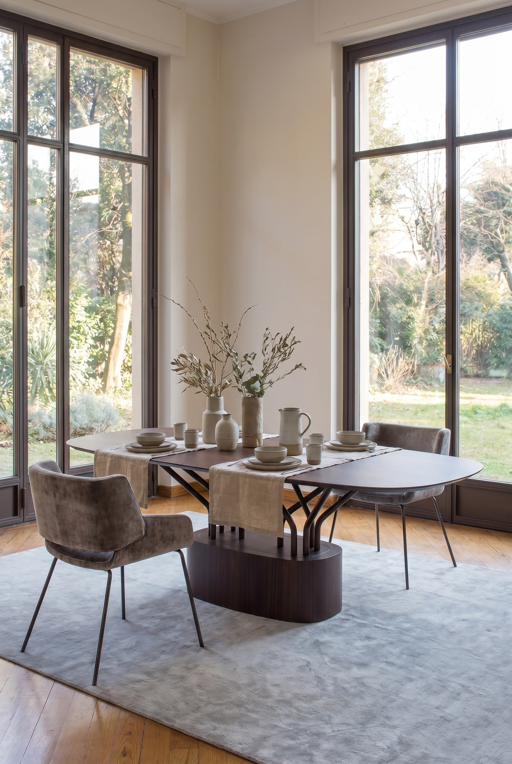 Moderne eetkamer met opvallende houten tafel, waarvan de poten een open roosterstructuur vormen, met grijze gestoffeerde stoelen