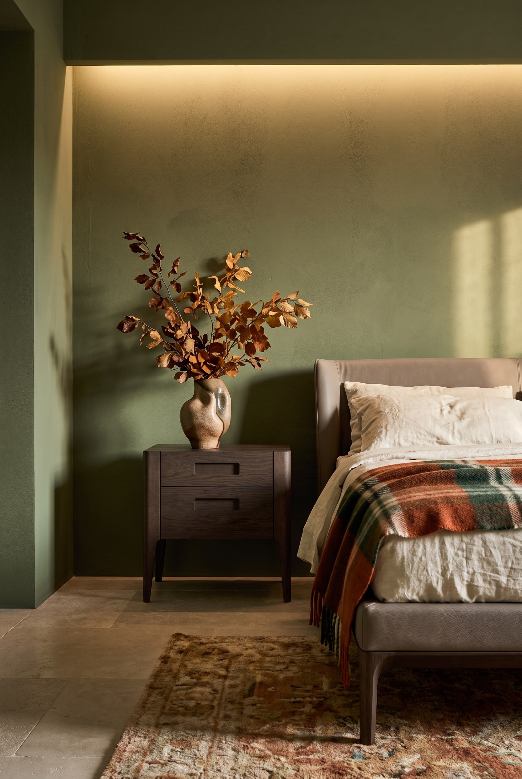 Een donker notenhouten nachtkastje met twee laden staat stijlvol voor een mat-olijfgroene muur in een elegante herfst-slaapkamer.