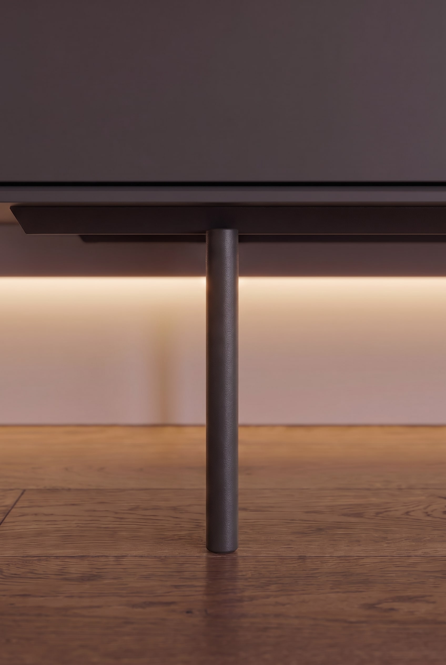 Nahaufnahme eines schmalen, zylindrischen Metallfußes eines Sideboards mit indirekter Unterbodenbeleuchtung auf Holzparkett.
