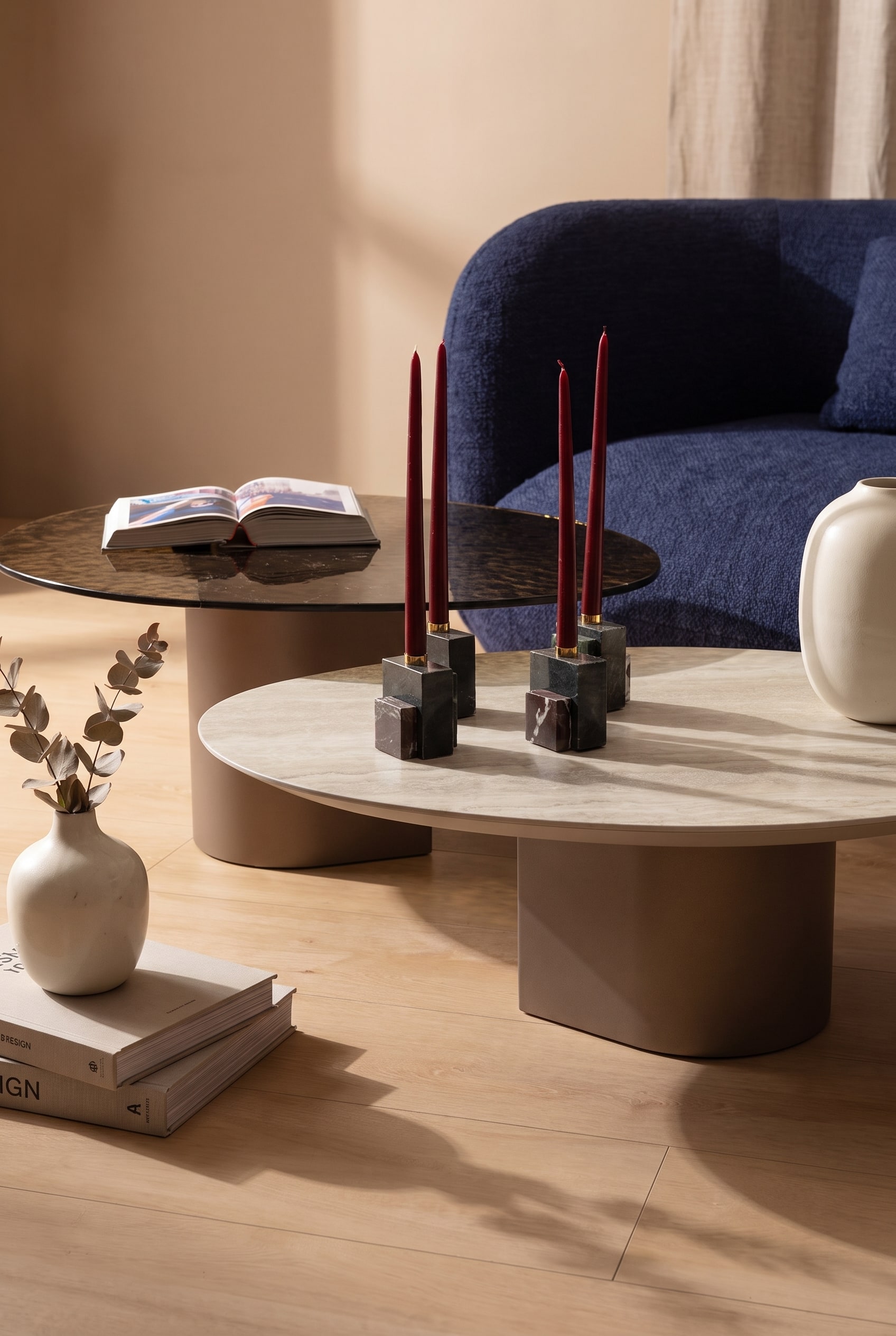 Close-up van een ronde salontafel van licht hout met keramische decoratie voor een donkerblauwe stoffen bank