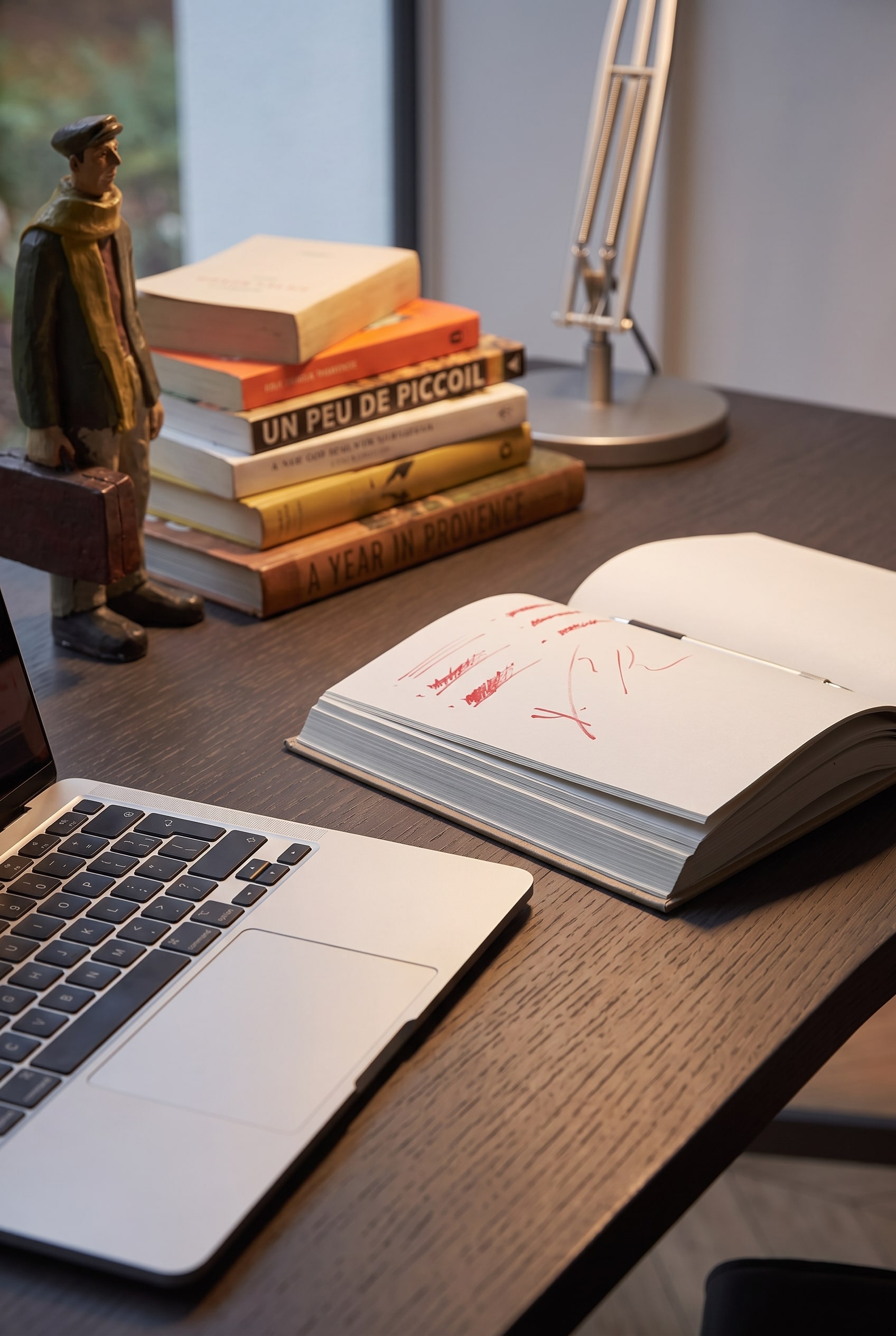 Makroaufnahme der schwarzen Eichenholz-Tischplatte mit aufgeschlagenem Notizbuch und Laptop-Tastatur.