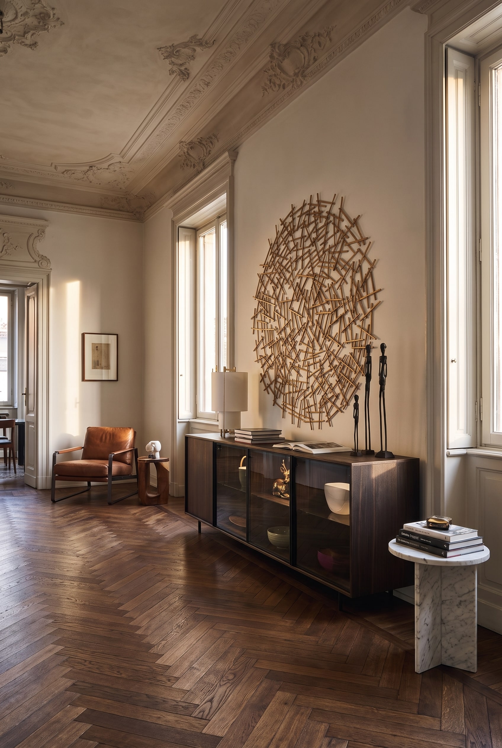 Una credenza in vetro allungata su piedini in metallo nero contro una parete in una stanza d'epoca, sotto la quale il parquet a spina di pesce in rovere continua ininterrotto.