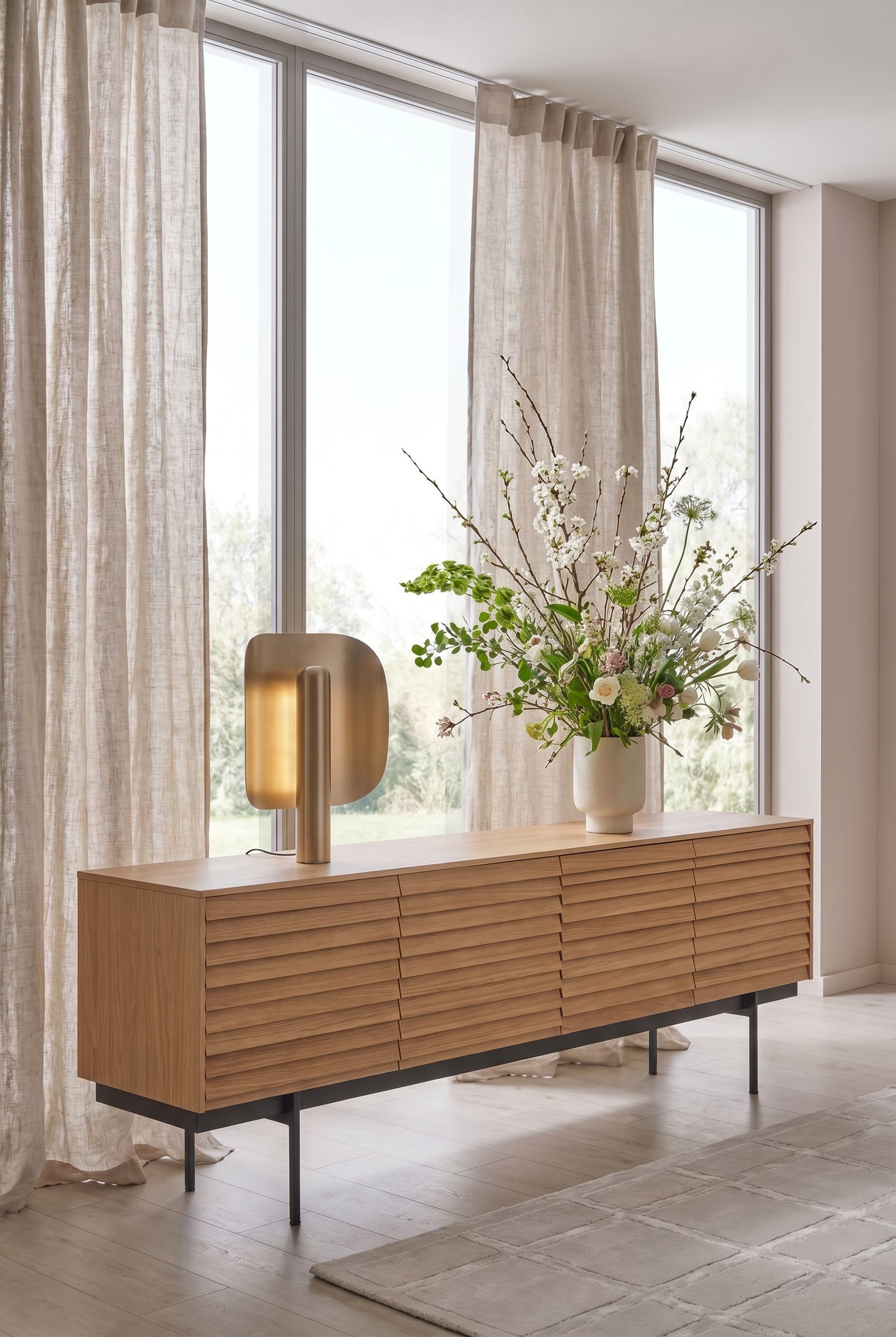 Minimalistisches Wohnzimmer mit einem Sideboard mit Holzlamellen, darauf ein gro&szlig;es asymmetrisches Fr&uuml;hlingsbouquet
