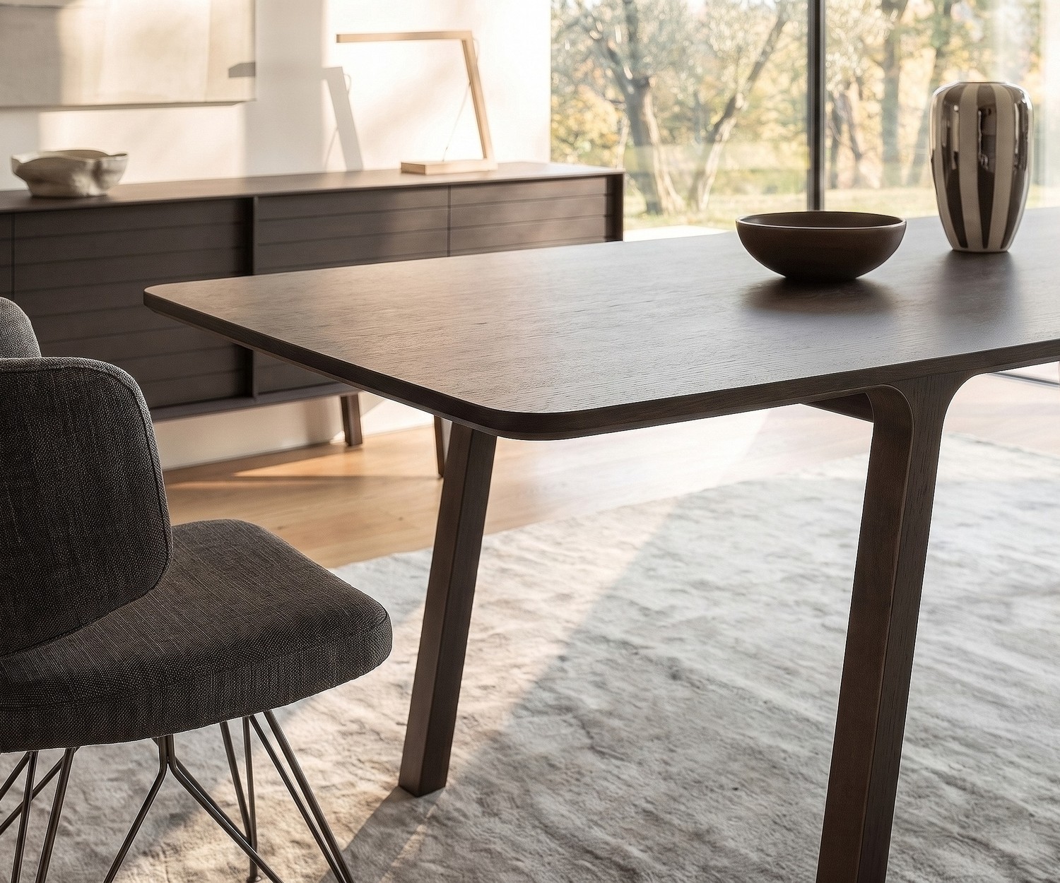 al2 mobius 001 Design Esstisch aus Eukalyptus Esstisch mobius 001 von al2 aus dunklem Eukalyptusholz im modernen Esszimmer mit passendem Design-Stuhl und hellem Teppich.