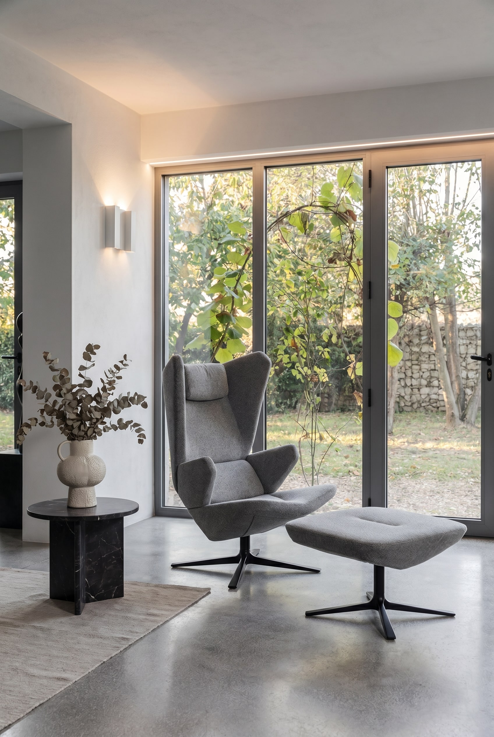Soggiorno moderno con poltrona Trifidae in tessuto strutturato grigio, tavolino con vaso in ceramica e ampie finestre