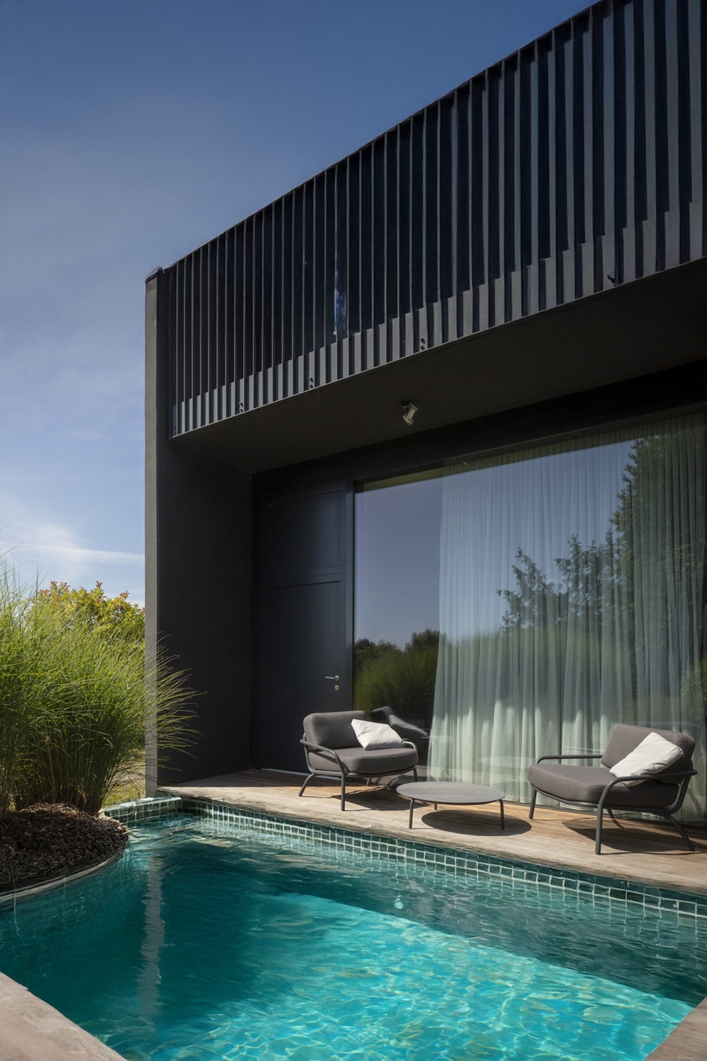 moderne-breite-polstersessel-mit-tisch-hinter-einem-pool