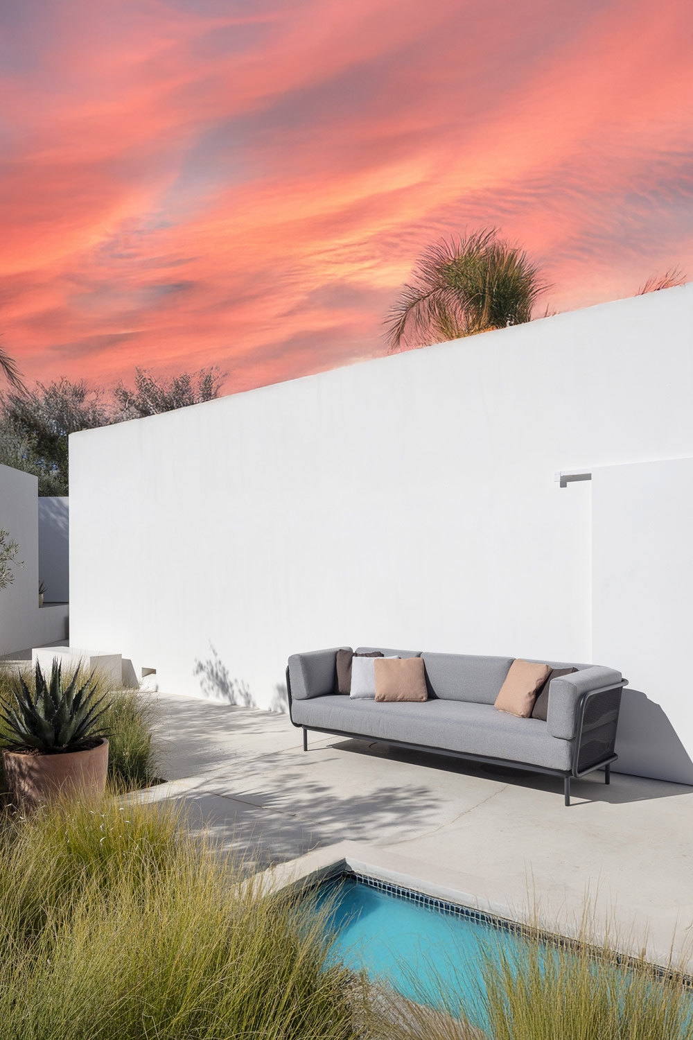 minimalistisch-designtes-komfortsofa-mit-runden-rueckenpolstern-auf-einer-mediterran-eingerichteten-terrasse-mit-pool