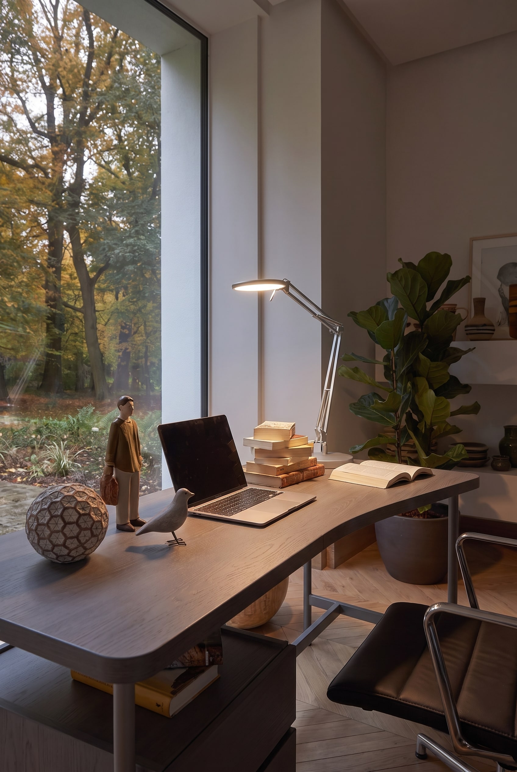 Beleuchteter Arbeitsbereich auf dem Schreibtisch mit glänzender Chromlampe, Holzfiguren und Laptop.