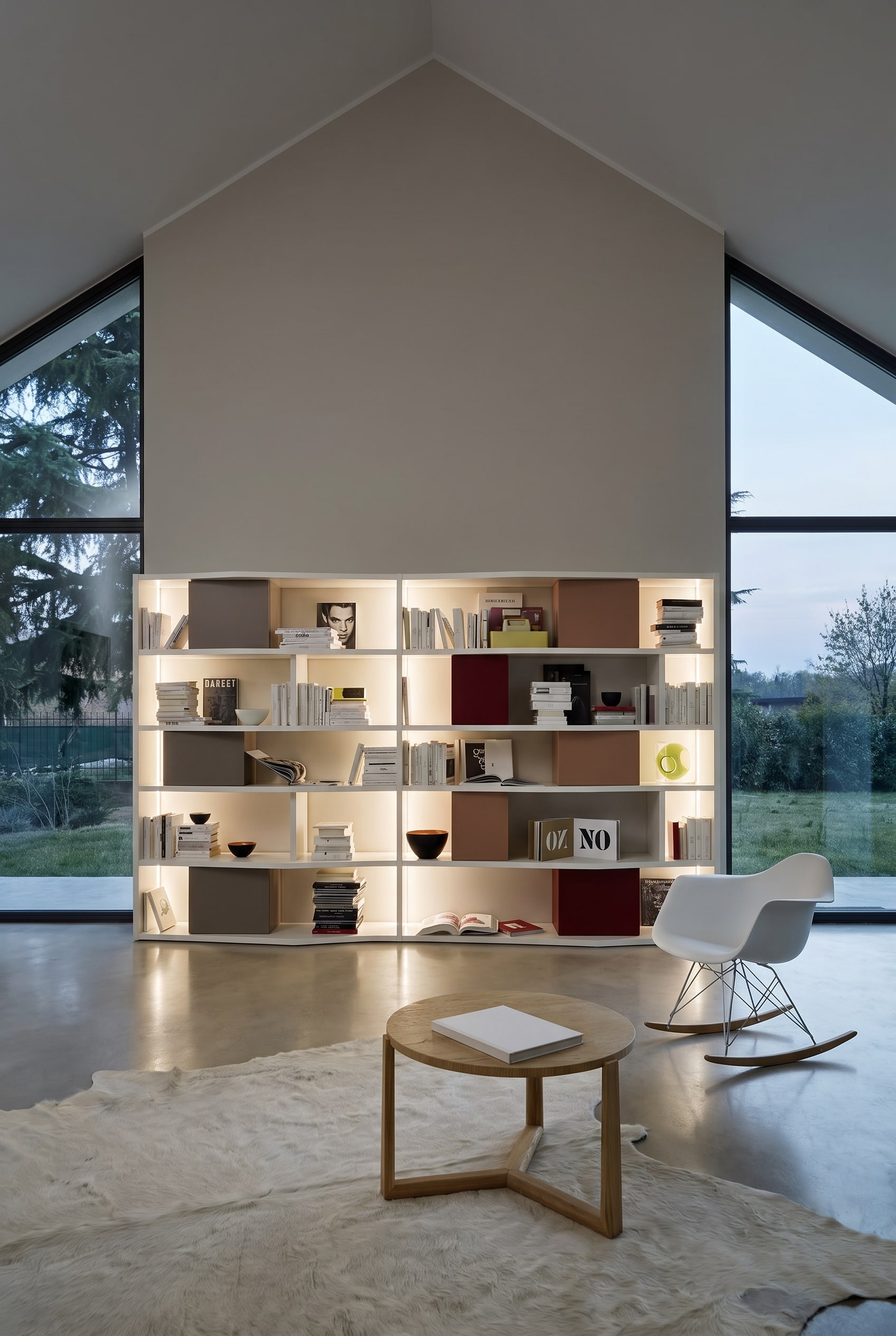 Hoge, witte boekenkast tegen een rechte gevelwand op zolder, gevuld met boeken en gekleurde opbergdozen