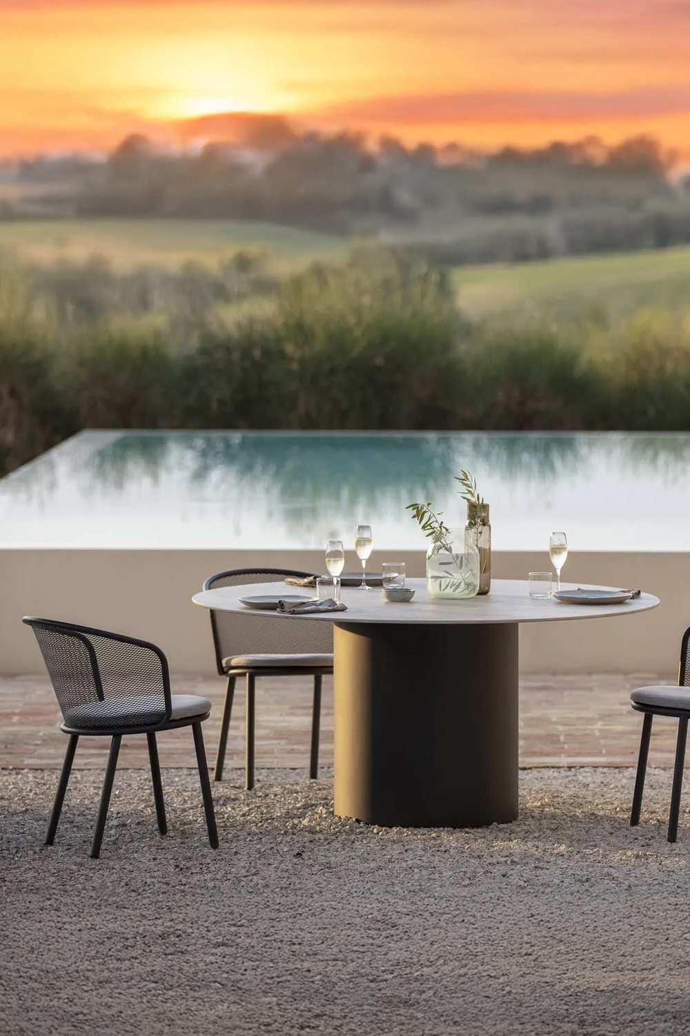 runder-gartentisch-mit-modernen-stuehlen-vor-grossem-swimming-pool