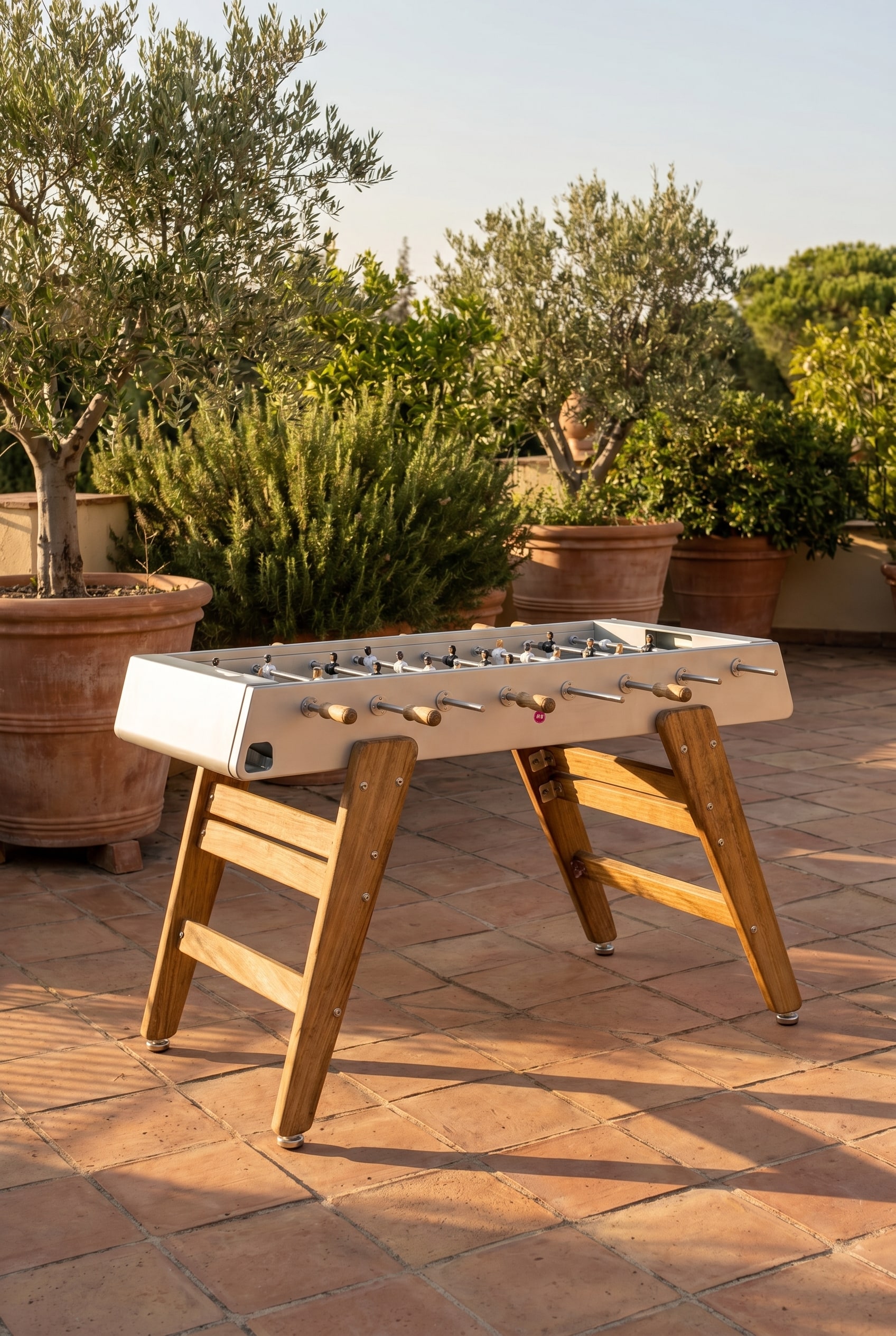 Mediterrane terras met Iroko-houten tafelvoetbaltafel en grote plantenbakken in het warme avondlicht