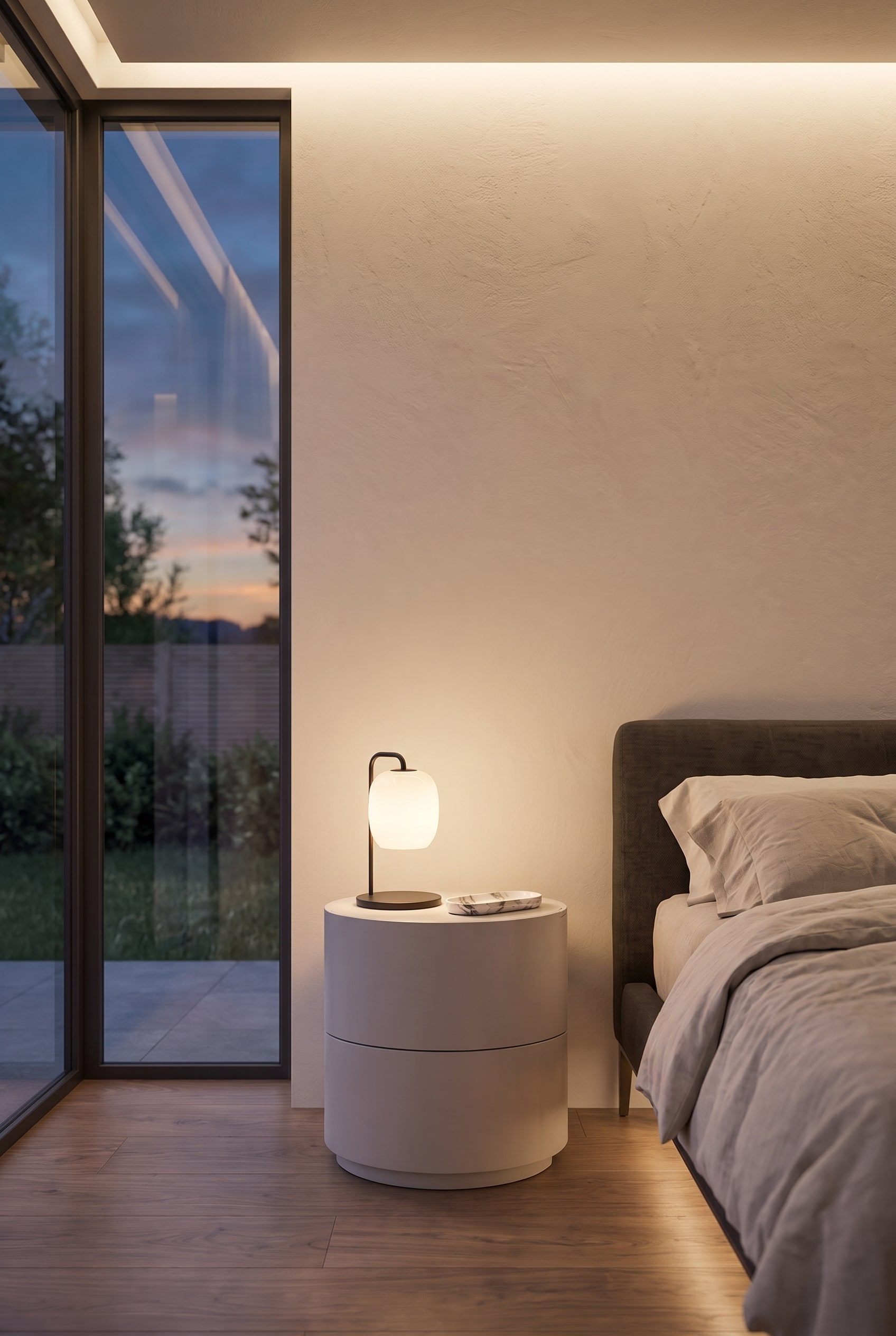Cilindervormig, mat nachtkastje met twee laden direct naast een modern gestoffeerd bed.