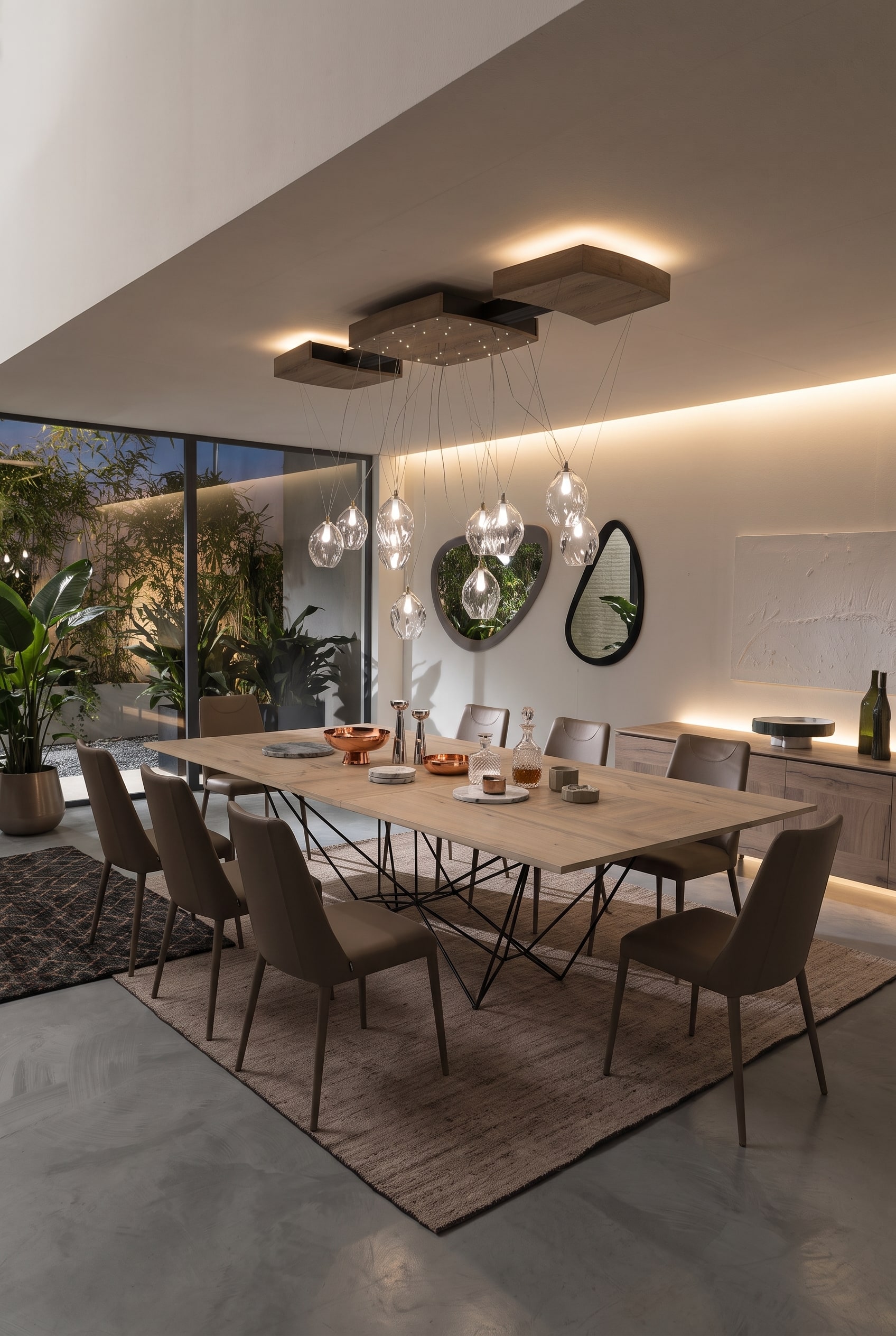 Sala da pranzo moderna e aperta con grande tavolo da pranzo su base metallica geometrica, quattro sedie color tortora e credenza in legno