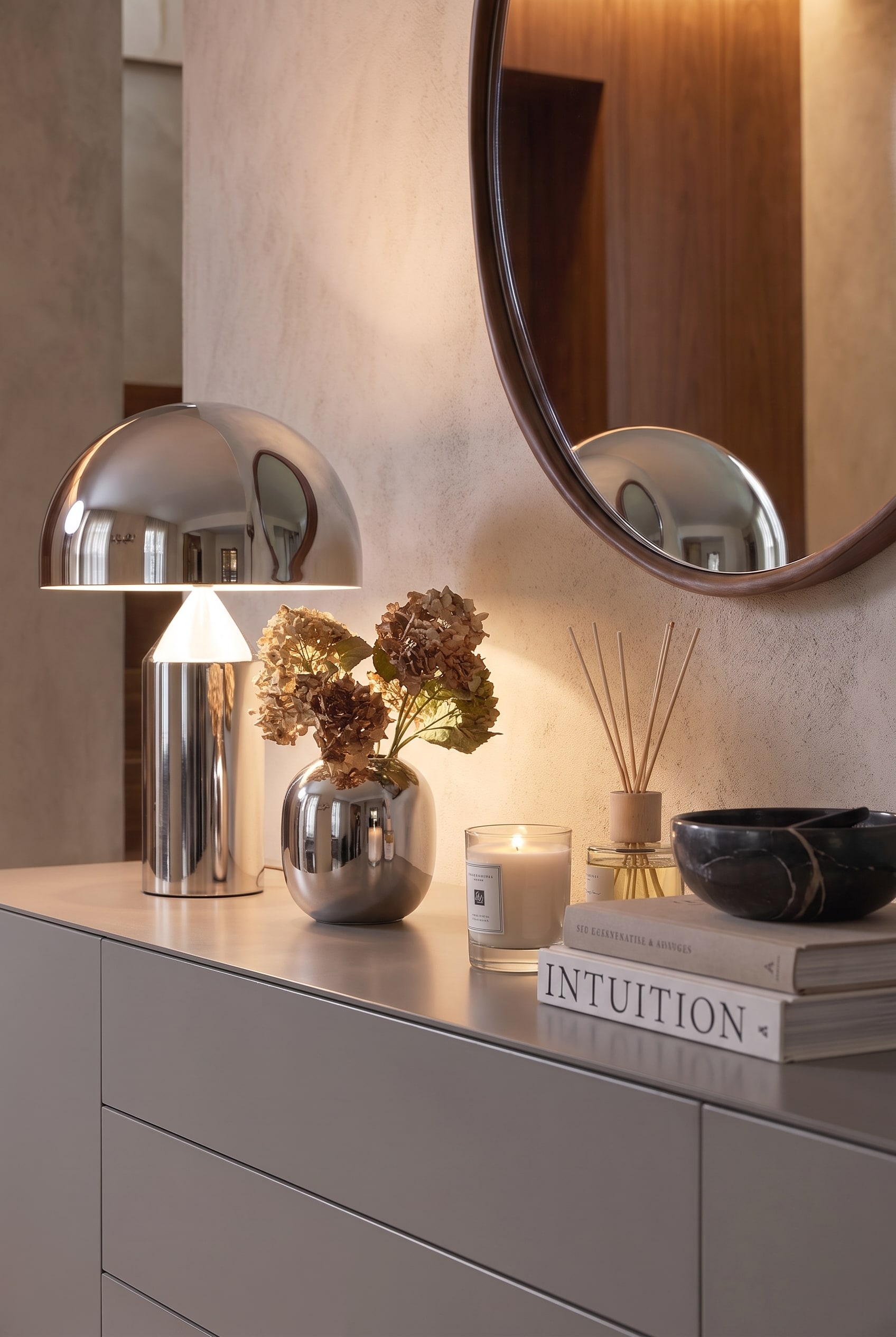 Close-up van decoratie: Een glanzende chroomlamp, een zilveren vaas met gedroogde hortensia's en een brandende kaars op grijs lak.