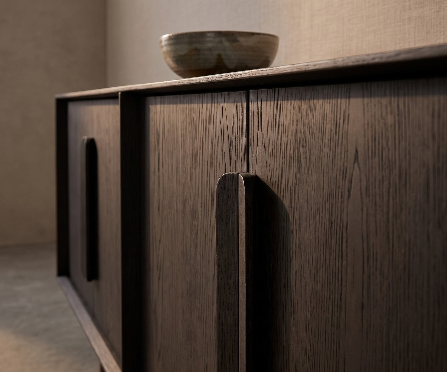 al2 Mobius 003 Sideboard aus dunkler Carbone Eiche im Wohnzimmer mit edlen Holzgriffen und dekorativer Schale im Detail.