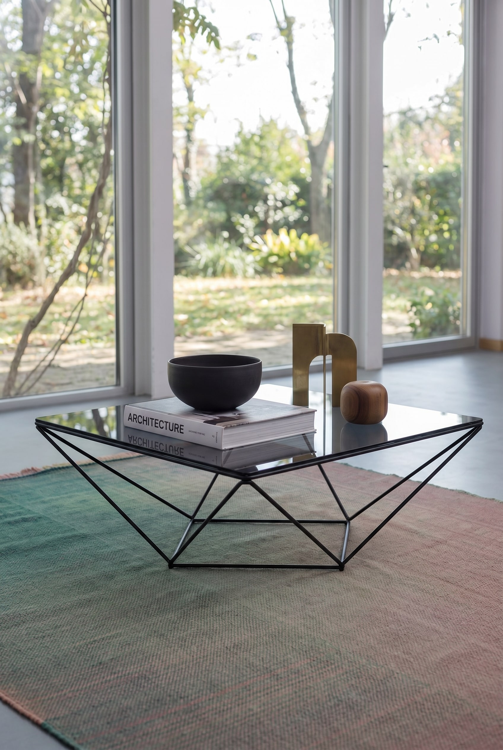 Luchtige woonkamer met vierkante glazen salontafel met fijn metalen frame, daarop een architectuurfotoboek en een donkere keramische schaal