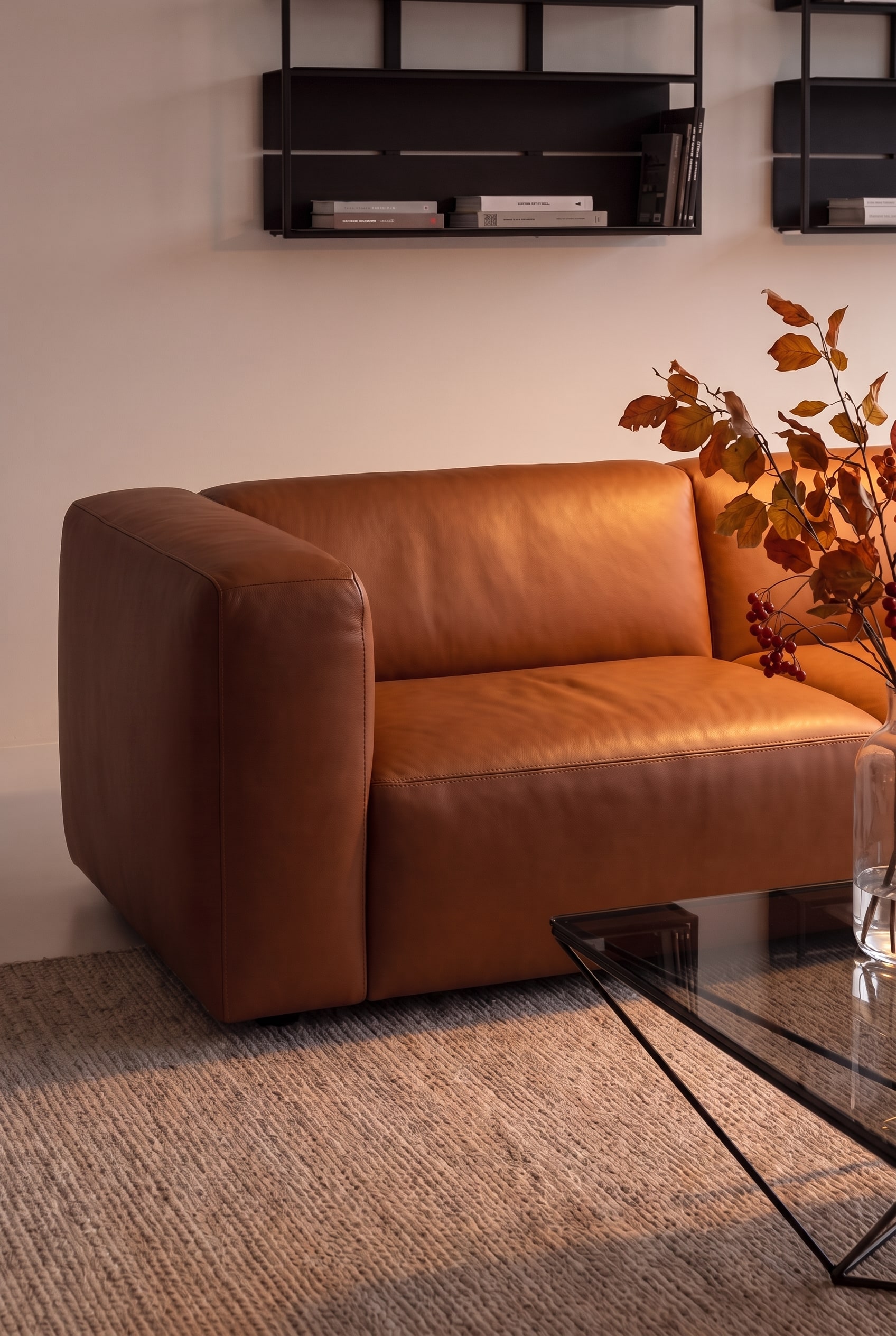 Primo piano del bracciolo liscio e senza cuciture di un divano in pelle color cognac, illuminato da luce calda.
