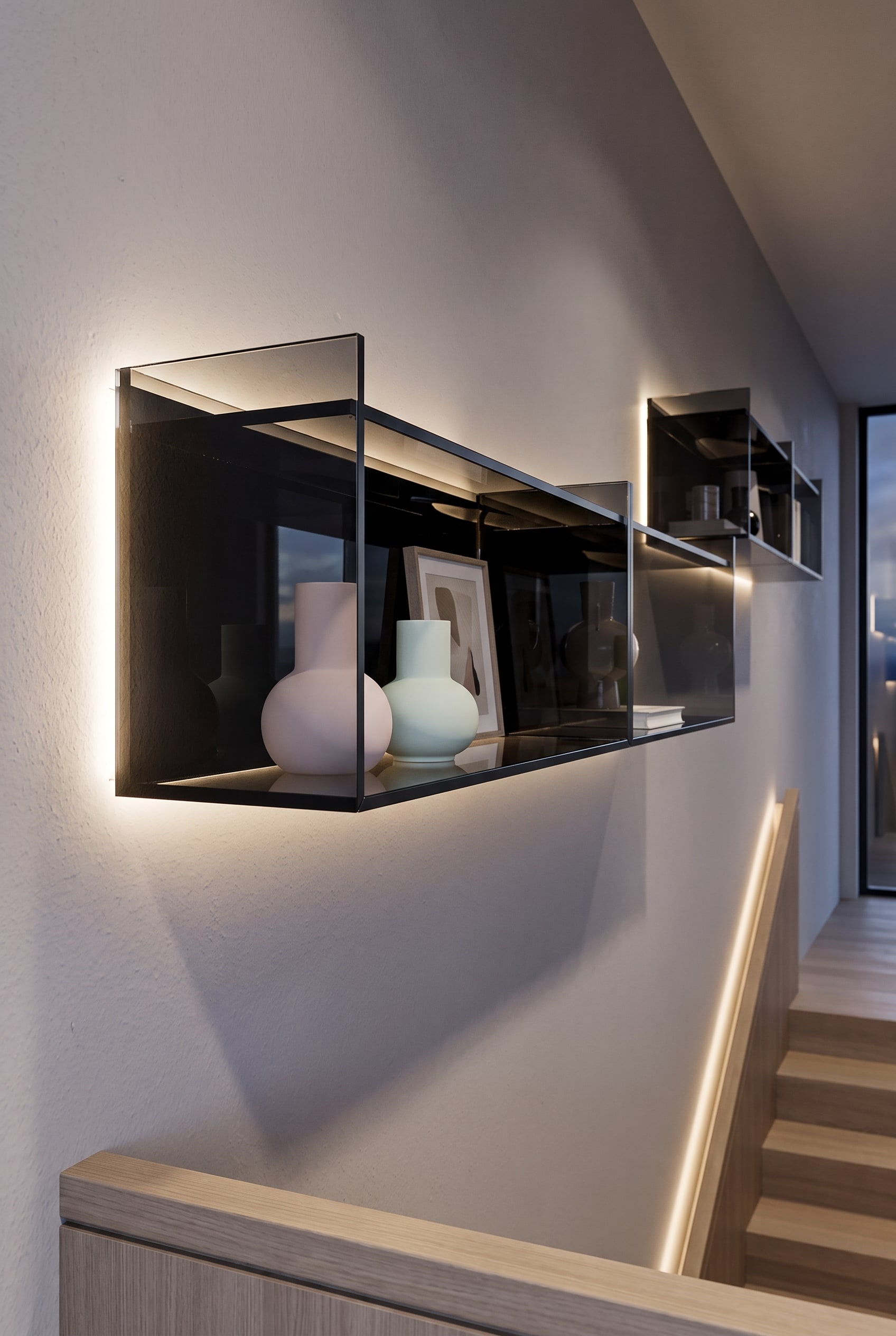 Zwevend glasrek aan een donkere muur in het trappenhuis, voorzien van lichte vazen en kunstobjecten