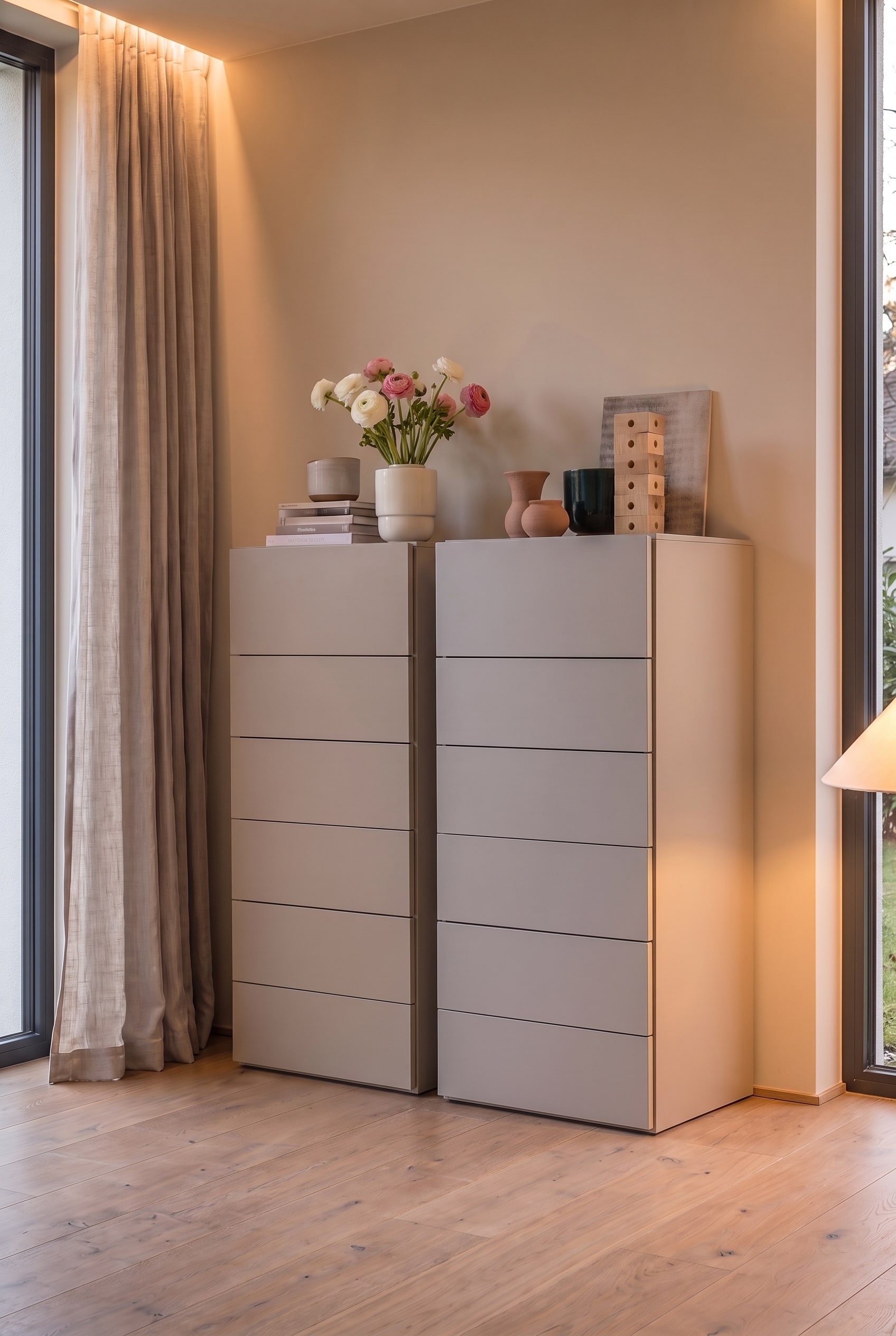 Twee identieke greige hoge ladekasten naast elkaar in de slaapkamer, verlicht door warm omgevingslicht.