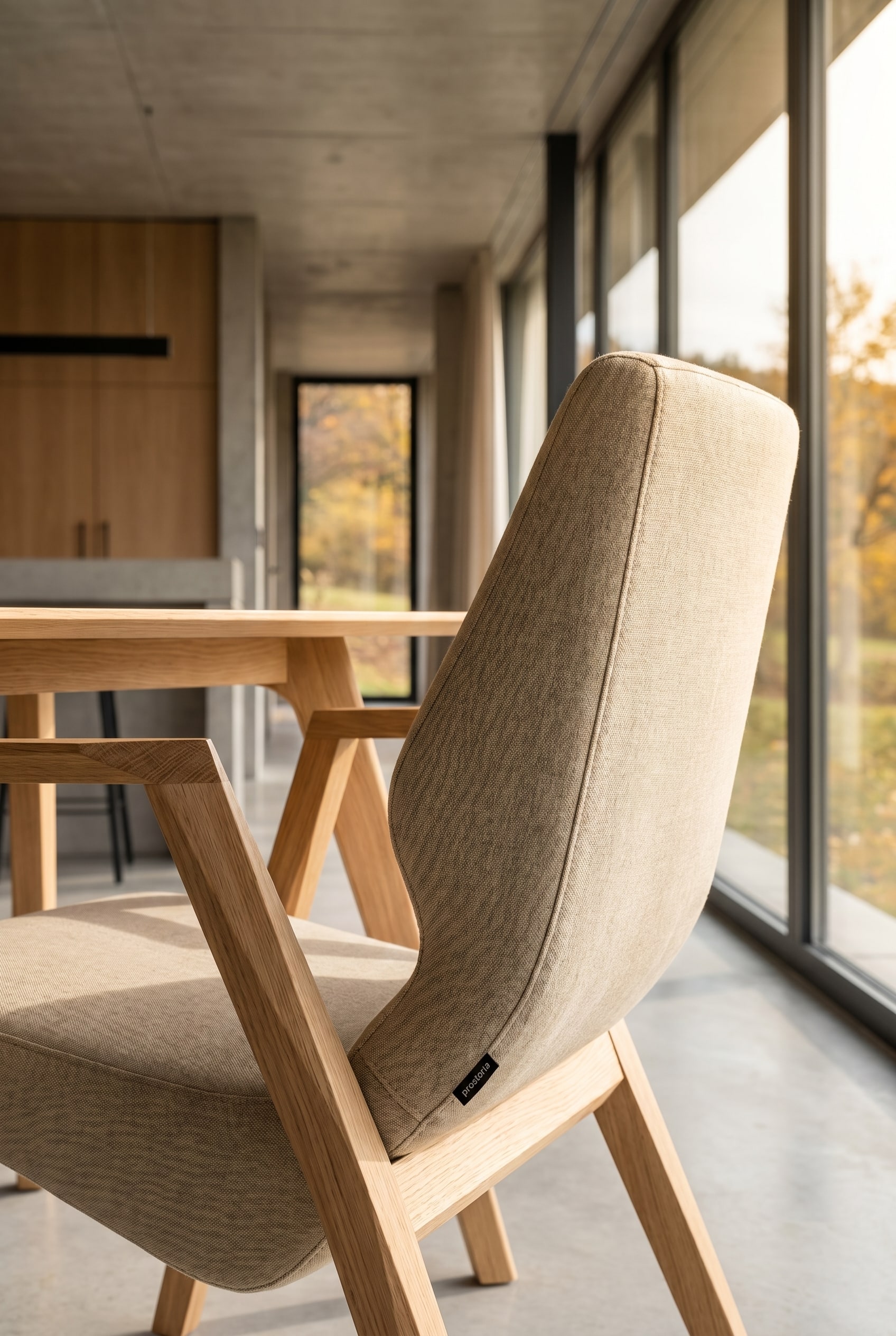 Elegant dining room with a Prostoria Oblique Sessel with wooden frame at the head of the table in front of floor-to-ceiling windows
