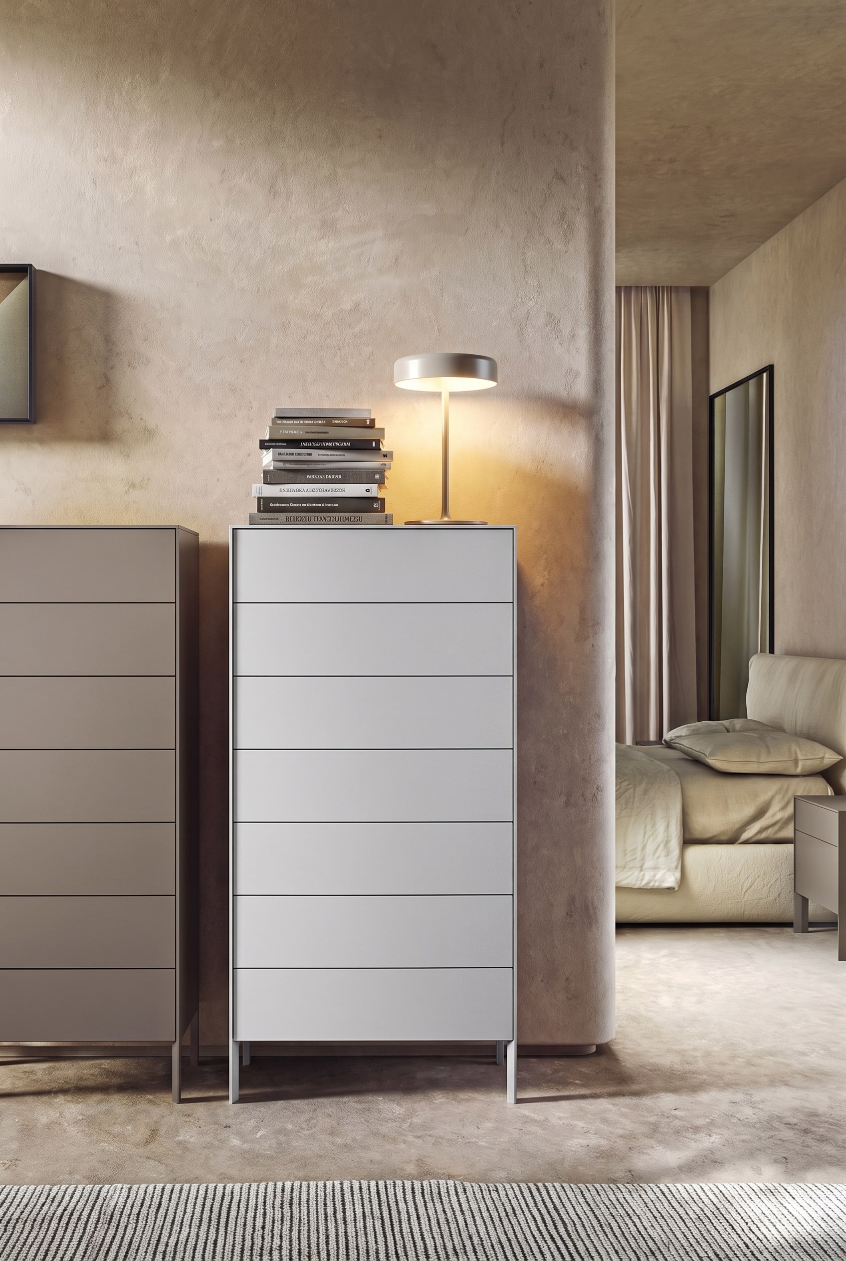 Minimalist bedroom with tall gray dresser, massive stack of books and table lamp on the left side, right side empty