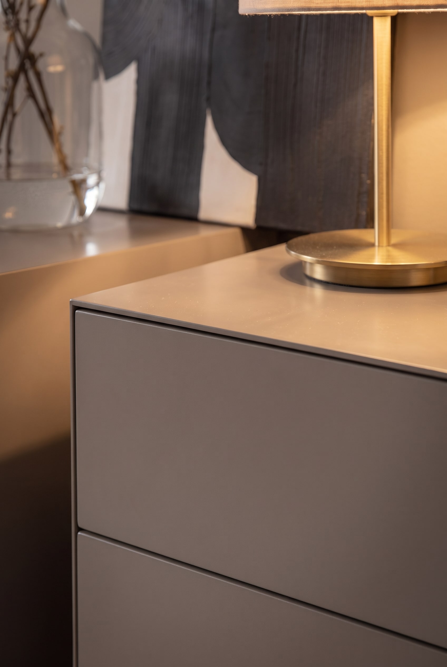 Primo piano del bordo di una cassettiera di design grigia opaca con una base di lampada color ottone.