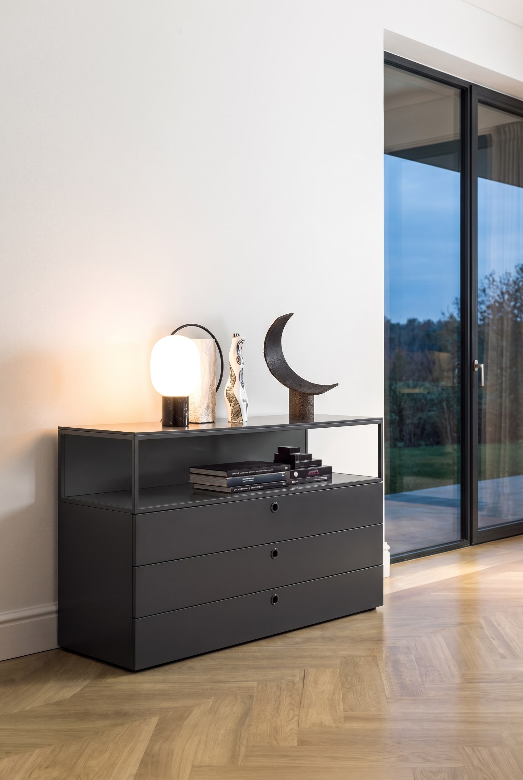 Modern living room with deep black matte chest of drawers in front of a white wall on a light wooden floor