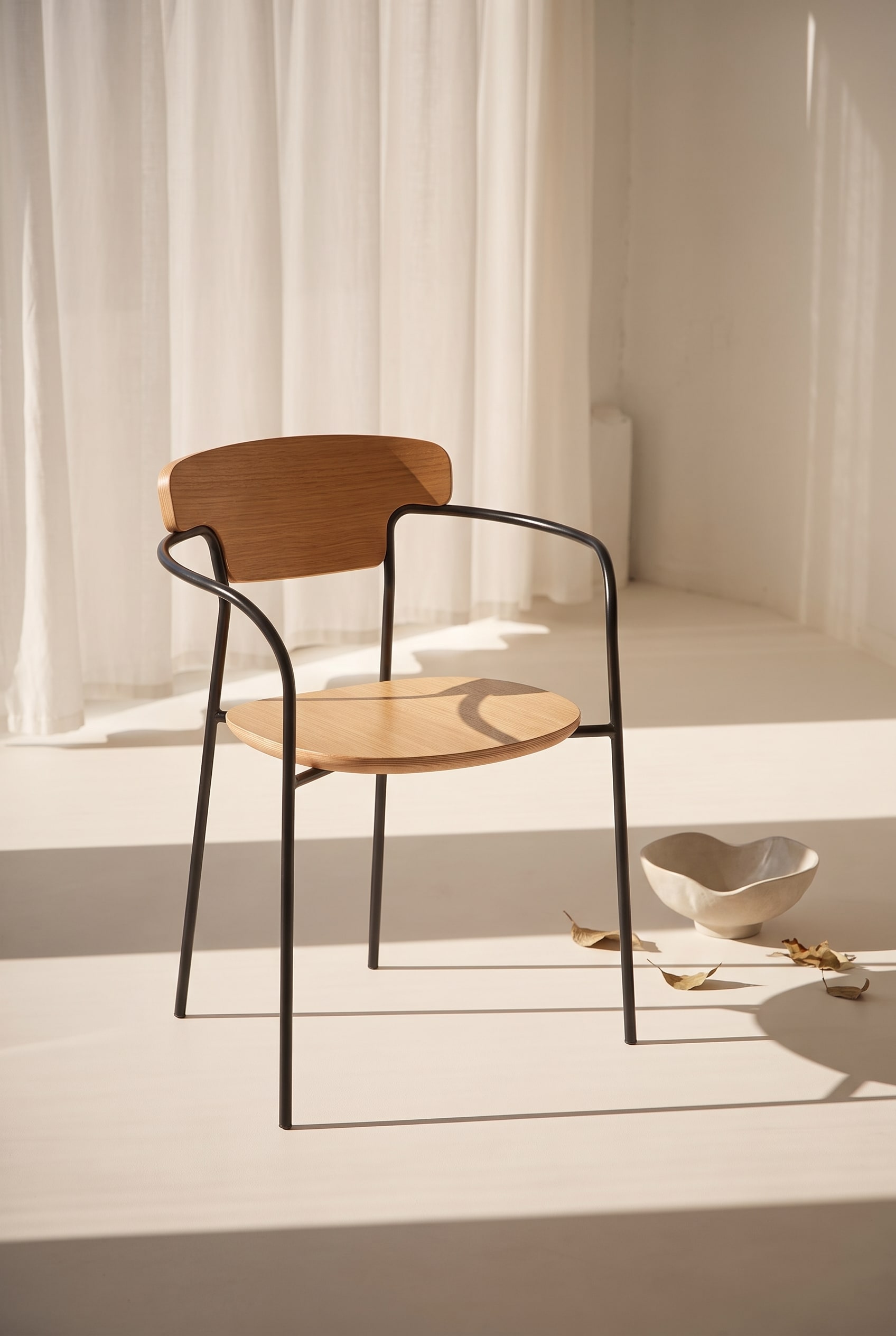 Stanza inondata di luce con una sedia da pranzo in legno di quercia con schienale curvo e struttura in metallo nero