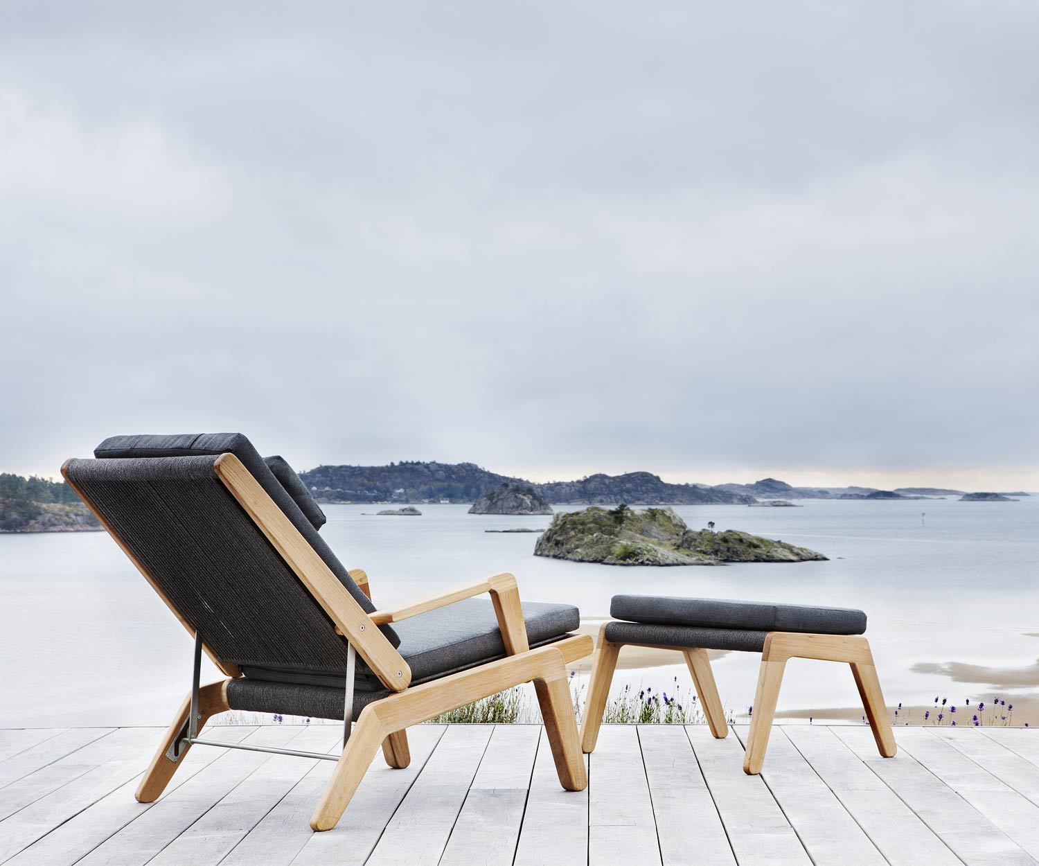 Oasiq Skagen design stool with upholstered cushion in dark grey in front of deckchair