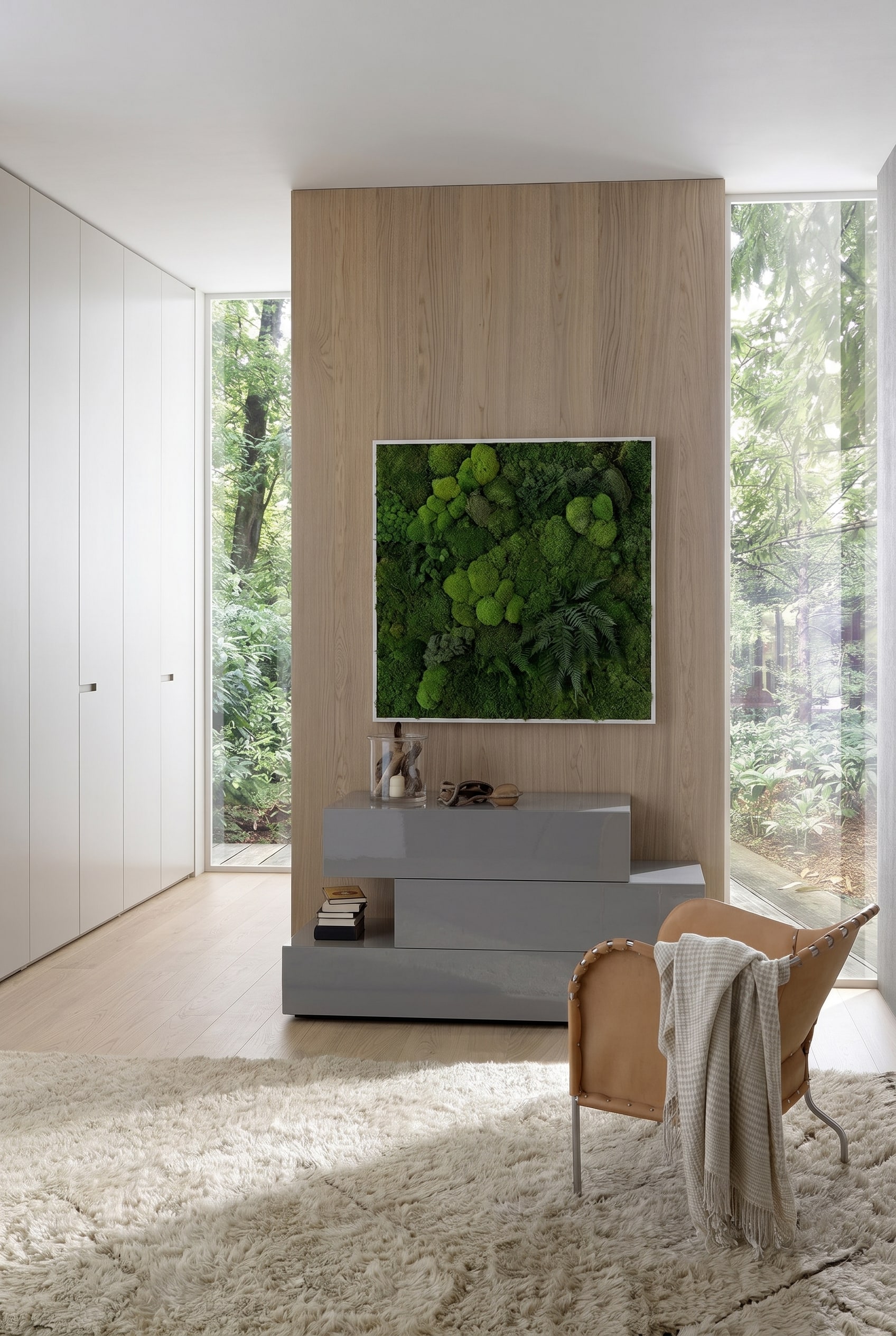 Camera da letto moderna con cassettiera grigia asimmetrica lucida, sopra un quadro di muschio incorniciato e una poltrona in pelle