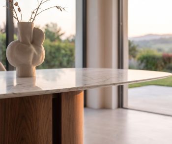 al2 el-it c 001 dining table in a modern dining room featuring a white marble-look top, wooden pedestal base and vase.
