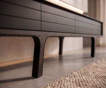 al2 Mobius 004 TV lowboard in a living room featuring smoked eucalyptus wood legs and matte dark grey cabinet doors.